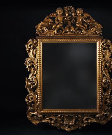 Specchiera in legno dorato con cornice riccamente scolpita a volute fogliate...