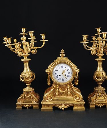 Trittico in bronzo dorato composto da una pendola e una coppia di flambeaux....