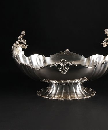 Centrotavola in argento. Corpo ovale sbalzato a costolature, arricchito da...