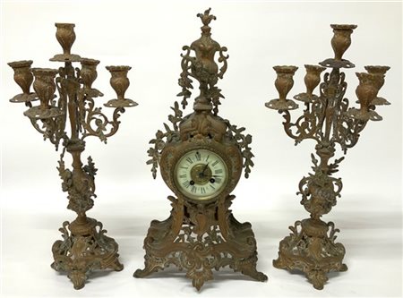 Trittico in metallo formato da una pendola e due candelabri. Quadrante a fascia