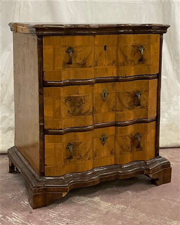 Comodino lastronato e filettato con fronte mosso a tre cassetti. Piedi a mensol