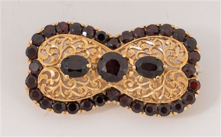 Spilla in oro giallo 18k realizzata a fiocco decorato da granati. Peso...