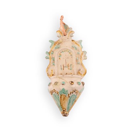 Manifattura dell'Italia centro-meridionale del XIX secolo ( - ) 
Acquasantiera in maiolica con decori in rilievo e monogramma cristologico HIS sormontato da una Croce. 
 cm 22x10