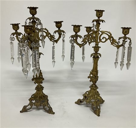 Coppia di candelabri in metallo dorato a quattro fiamme decorato a volute fogli