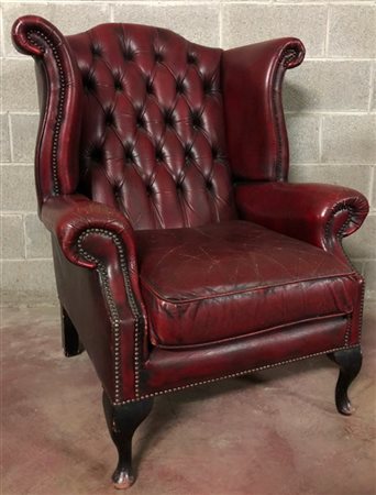 Poltrona a orecchioni rivestite in pelle bordeaux borchiata con gambe in legno