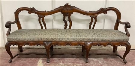 Divano in legno intagliato di forma mossa con decoro a volute e motivi fogliace