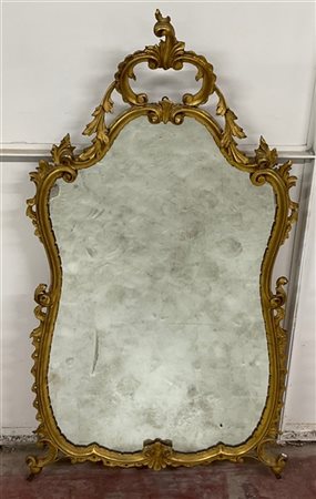 Specchiera di forma mossa in legno intagliato e dorato a volute con cimasa traf