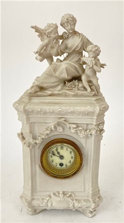 Orologio da tavolo con cassa in porcellana sormontata da figure di amorini e donna, quadrante in smalto a numeri arabi. Fine secolo XIX (h. cm 32) (difetti)