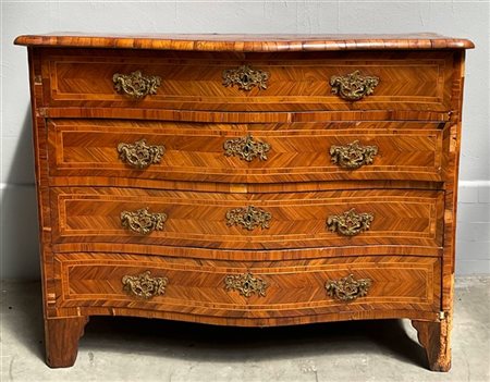 Comò di forma mossa lastronato e filettato con fronte a quattro cassetti, piedi