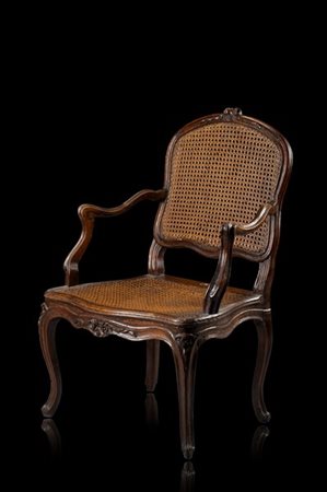 Poltrona di forma mossa in noce, fascia intagliata a motivi vegetali. Schienale