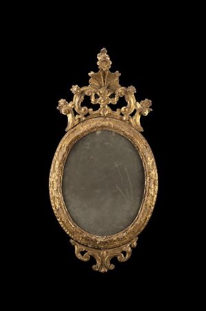 Specchiera di forma ovale in legno intagliato e dorato a volute e fiori, cimasa