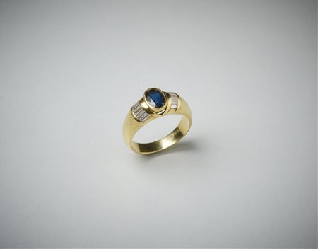  . - Anello in oro giallo 750/1000  a fascetta con zaffiro blu ovale di 0.70  ct ca. e diamanti bianchi laterali taglio a baguette di 0.75 ct totali circa.  .