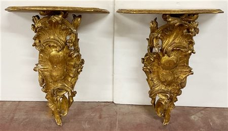 Coppia di console composte da sostegni in legno intagliato e dorato a volute e