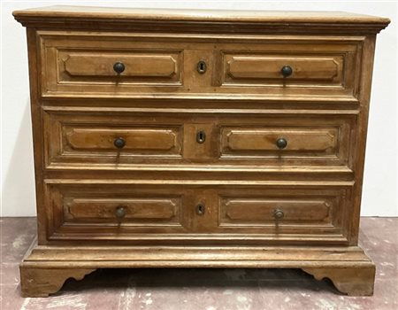 Antico comò in legni vari con fronte a tre cassetti pannellati, piedi a mensola