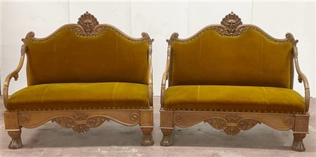 Coppia di divani a due posti intagliati con decoro a volute e cimasa con masche