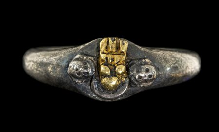AN EARLY MEDIEVAL SILVER RING WITH SKULL HEADS AND CENTRAL GILDED EMBLEMA.
