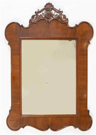 Specchiera lastronata in noce, di forma mistilinea con cimasa intagliata....