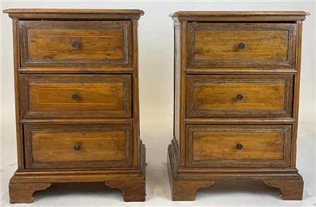 Coppia di comodini in legni vari a tre cassetti pannellati, piedi a mensola. Se