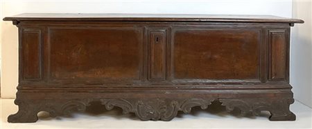 Cassapanca in noce con fronte e fianchi pannellati, grembiale intagliato a volu