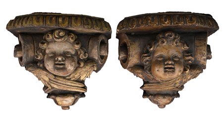 Coppia di mensole esagonali in legno finemente intagliato e dorato con testa di cherubino al fronte e decoro a volute mistilinee ai lati.    