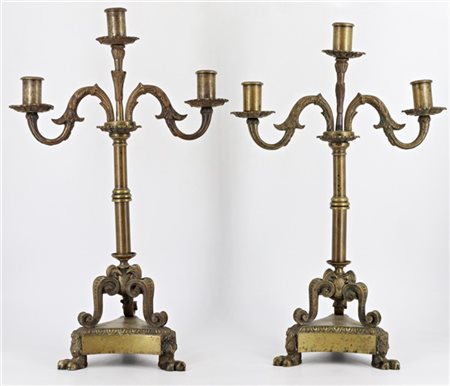 Coppia di candelabri in bronzo a tre fiamme con sostegno tripode a voluta su ba
