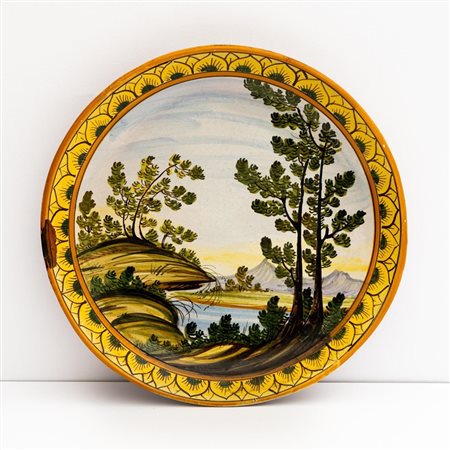 Piatto in maiolica decorato alla tesa con motivi fogliati alternati e nel cavo con ornato a paese    Manifattura di Castelli della metà del XX secolo