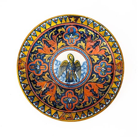 Piatto in maiolica decorato a lustro metallico. Nella tesa decoro alternato di triangoli con quattro stelle ai punti cardinali.  Manifattura di Gualdo Tadino del XX secolo