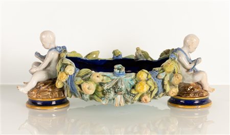 Centrotavola di gusto robbiano neoquattrocentesco con ai lati due putti in maiolica bianca modellati a tutt tondo che trattengono una ghirlanda di frutta  