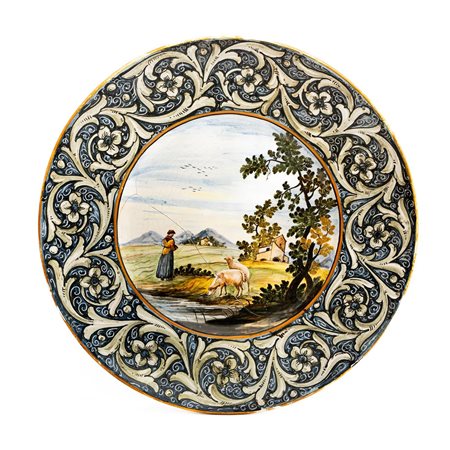 Grande piatto di Castelli. Manifattura Stella con decoro a girali fogliati sulla tesa e paesaggio agreste con donna e pecore sul greto del fiume   Manifattura di Castelli della metà del XX secolo