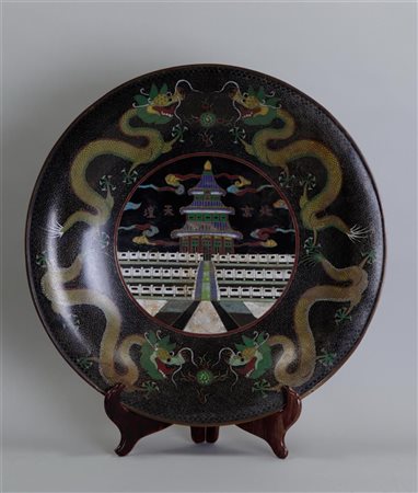 A large cloisonne dish decorated with dragons on the outer rim and a temple...