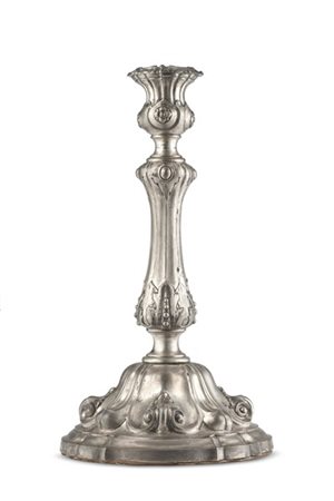 Candeliere in argento sbalzato con decori a volute e foglie su base mistilinea.