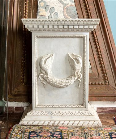 Base in marmo bianco statuario scolpito a mano dal blocco con decoro a rilievo di due uccelli stanti a trattenere tra le zampe un serto di alloro   