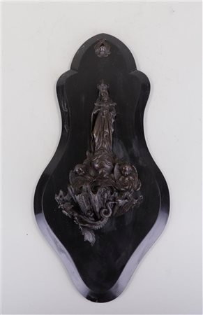 A bronze holy water font above which is the Virgin Mary with Christ Child....