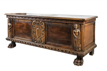 Cassapanca in legni vari con fronte decorato da intagli a figure e scudo, piedi