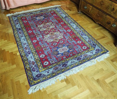 TAPPETO CAUCASICO fondo rosso, campo con motivi geometrici blu, giallo e...