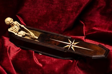 Memento mori raffigurante una bara ottagonale in legno di noce intarsiato con quattro piedini a cipolla contenente uno scheletro in avorio con arti snodabili. Nord Europa, metà secolo XIX