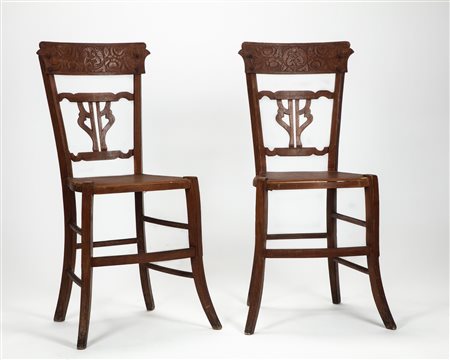 Coppia di sedie in legno con schienale traforato a giorno e fascia incisa a motivi vegetali. Gambe riunite da traverse. Secolo XX