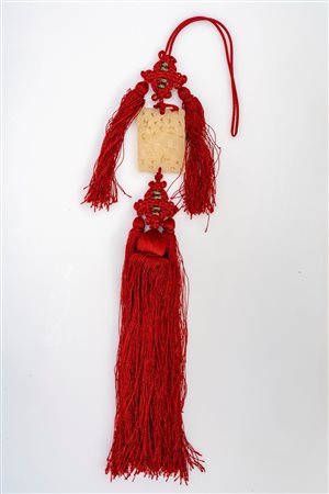 Placchetta in giada traforata raffigurante un cane di Fo, con nappe rosse. Cina, secolo XX