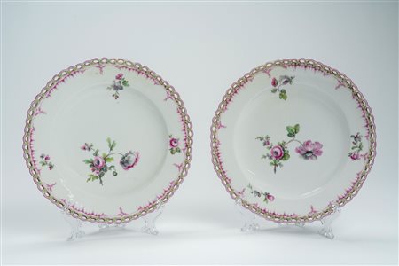 Coppia di piatti in porcellana a profilo traforato con fiorellini, decorati in policromia nei toni del porpora e del verde a rami di fiori. Manifattur […]