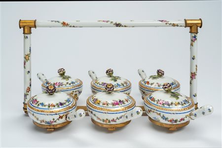 Servizio da tavola per salse e confetture in porcellana bianca parzialmente a rilievo, con decoro policromo a ghirlande di fiori e profili dorati. Ger […]