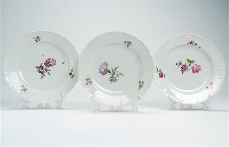 Tre piatti piani in porcellana a bordo mosso e a rilievo decorata in policromia a motivi floreali. Berlino, 1770 circa