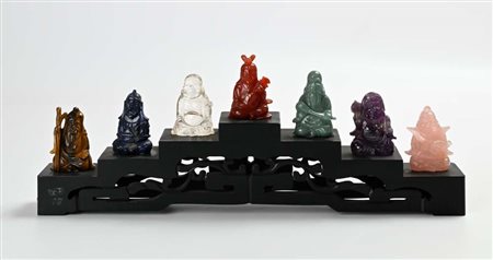 Sette piccole figure di saggio in pietra dura su base gradinata in legno...