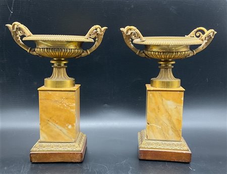 Coppia di alzate biansate in bronzo dorato a coppa baccellata su plinto rivesti