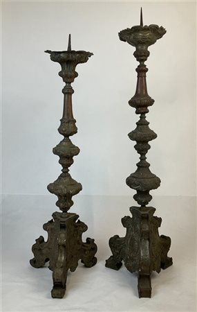 Due candelieri in legno rivestito in metallo argentato con base tripode. Secolo
