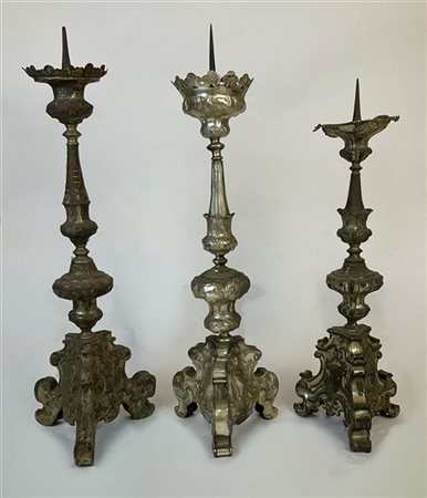 Lotto di tre candelieri in legno rivestiti in metallo argentato con decoro a vo