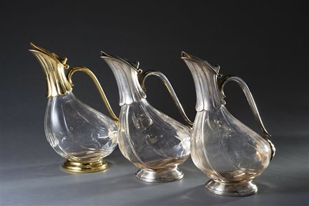 Gruppo di tre versatoi in vetro con ghiere e anse in metallo argentato e...