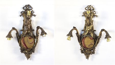 Coppia di appliques a tre fiamme con supporto centrale a forma di putto a...