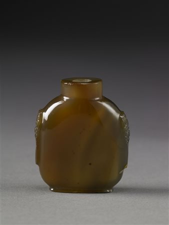 Snuff bottle in agata scura con marezzature, scolpita sui bordi a mascheroni...