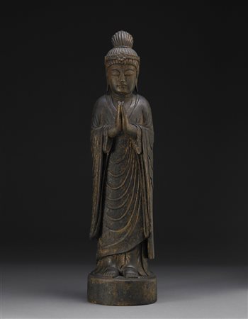 Scultura in legno intagliato raffigurante un Buddha stante, le mani giunte,...