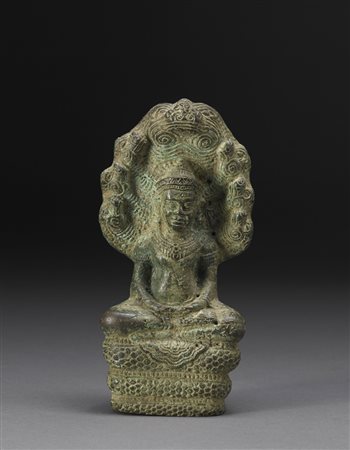 Divinità in bronzo seduta a gambe inrociate su un serpente a spirale, le mani...
